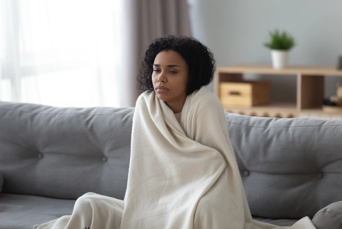 Lady sitting on couch wrapped in a blanket looking ill